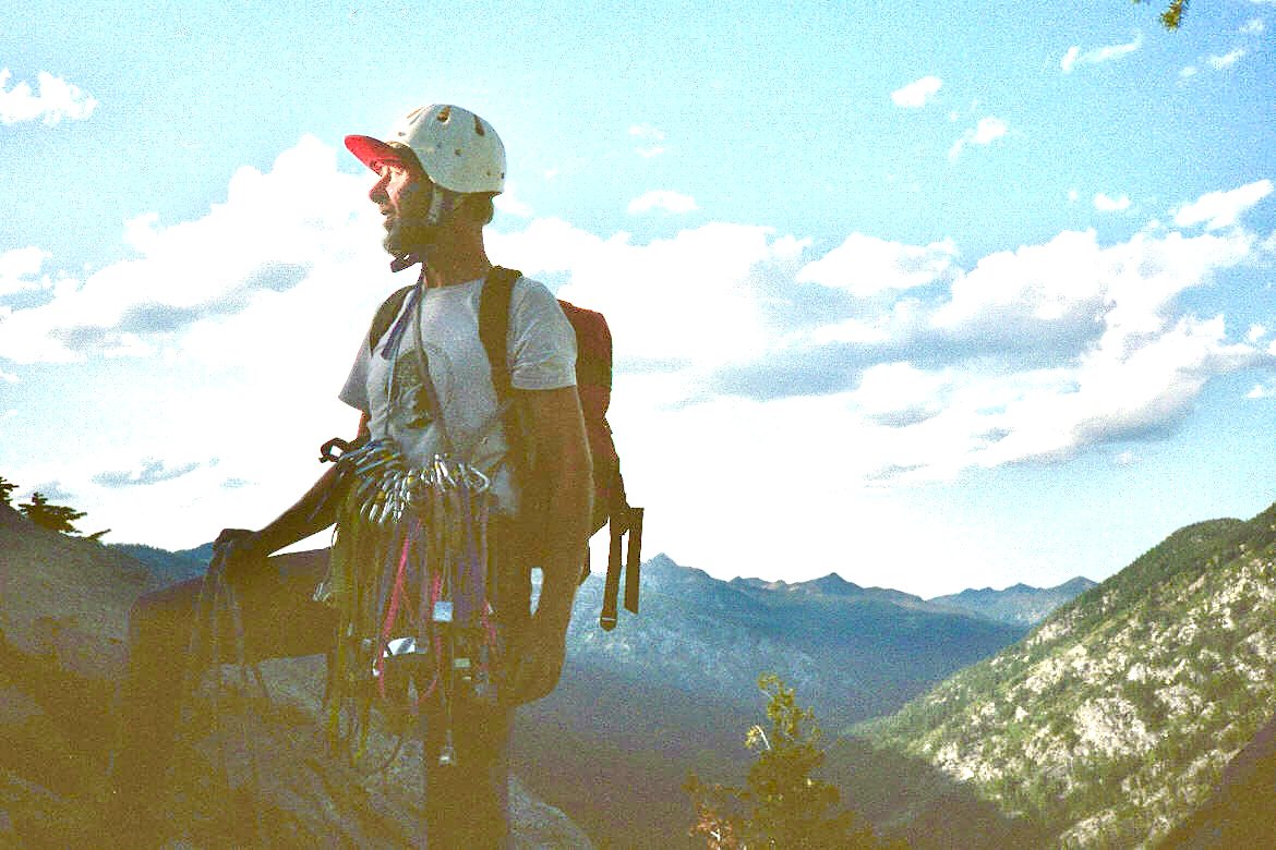 Tim carrying a climbing rack, rope, helmet, and backpack.
