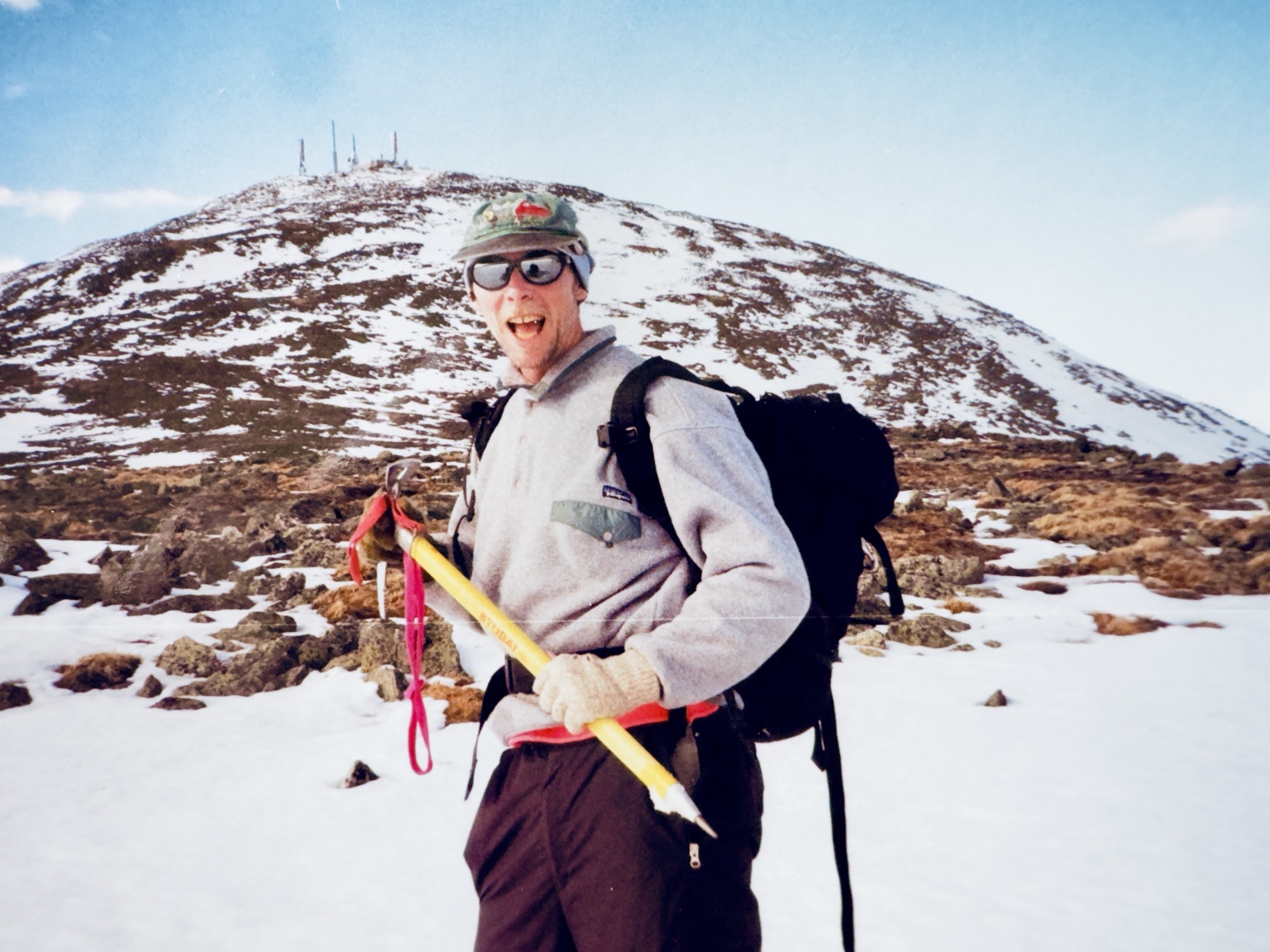 Tim hiking on a rocky, snow-covered mountain with an ice axe and winter pack