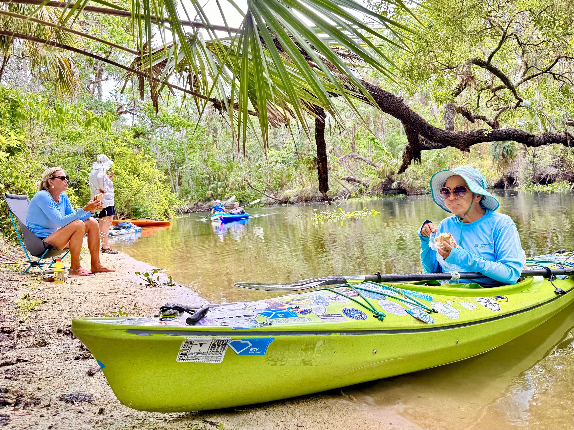 Paddlers resting beside a green kayak under palms