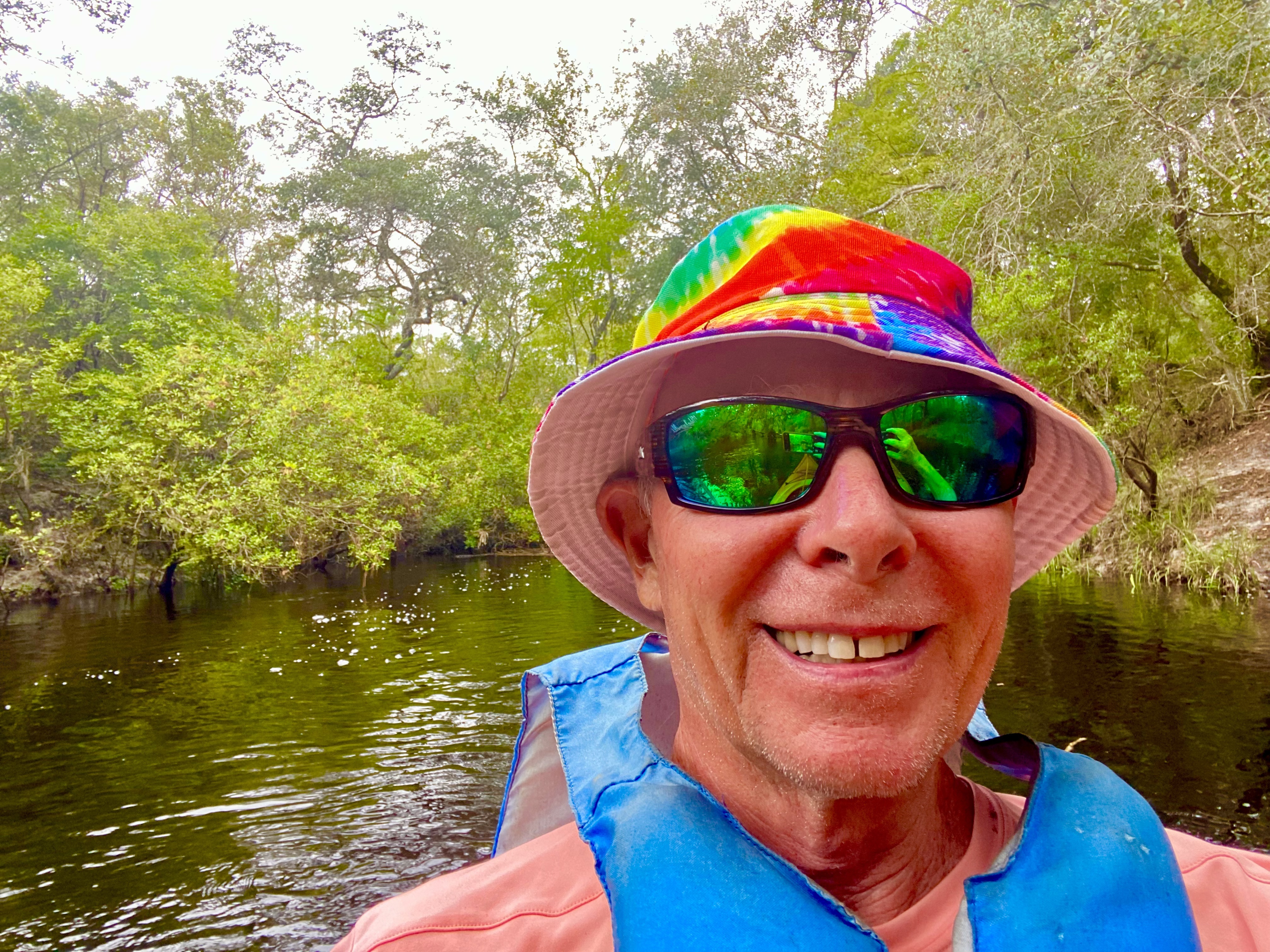 Tim smiling in his kayak while wearing a colorful hat on the Sopchoppy River