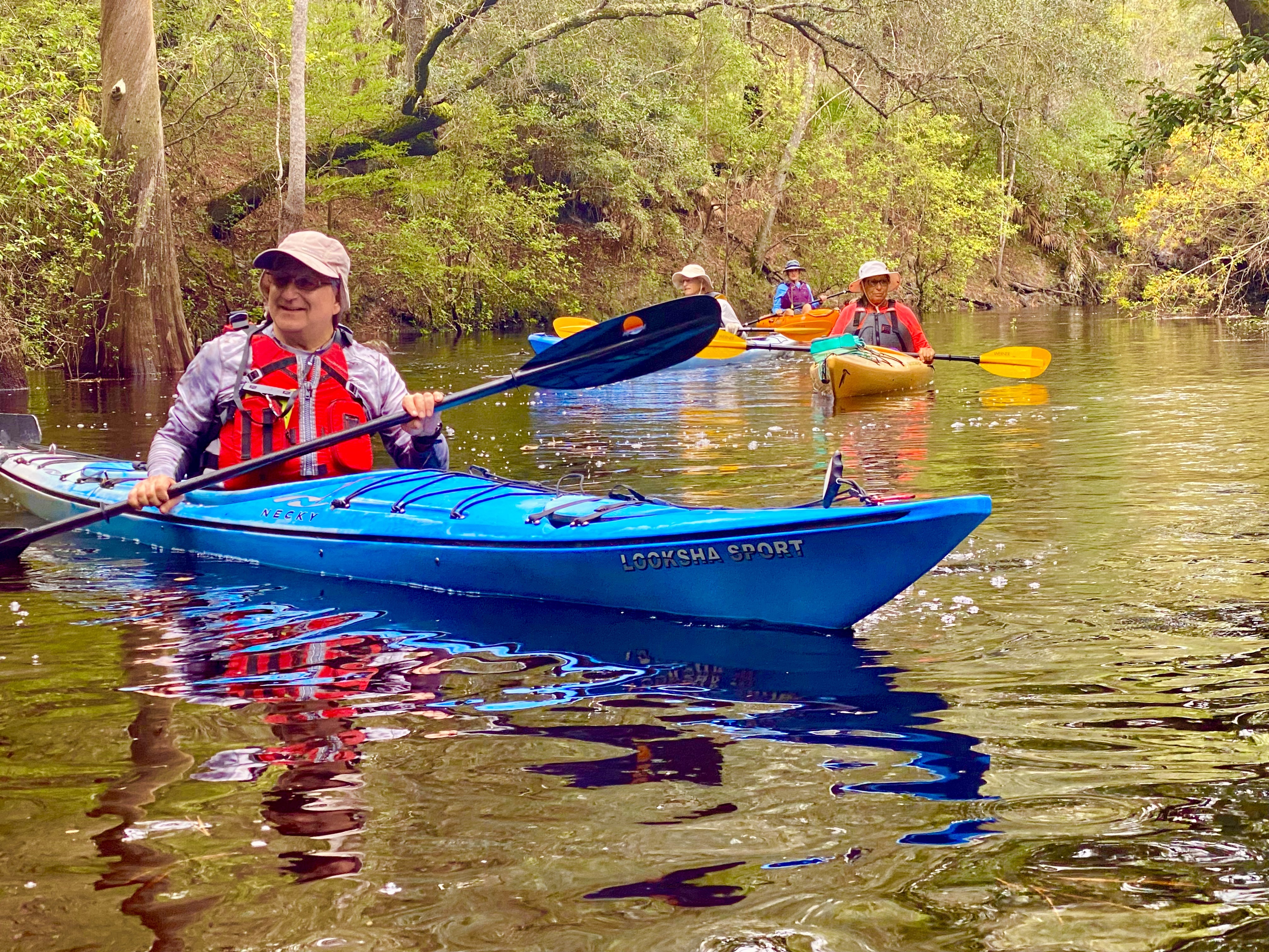 A woman in a blue kayak with other paddlers behind her on the Sopchoppy River