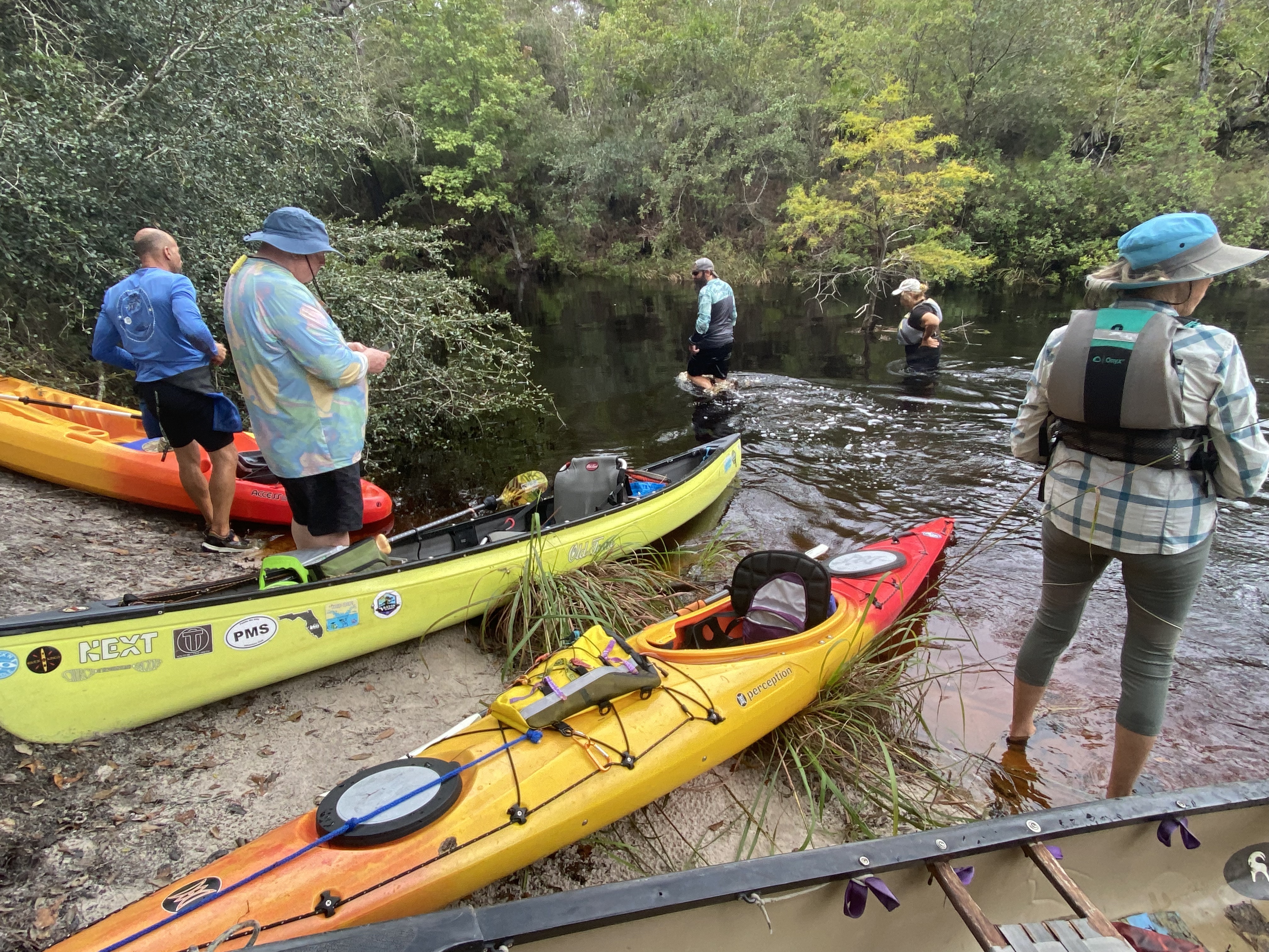 Paddlers and colorful boats gathered in shallow water at a sandy riverbank