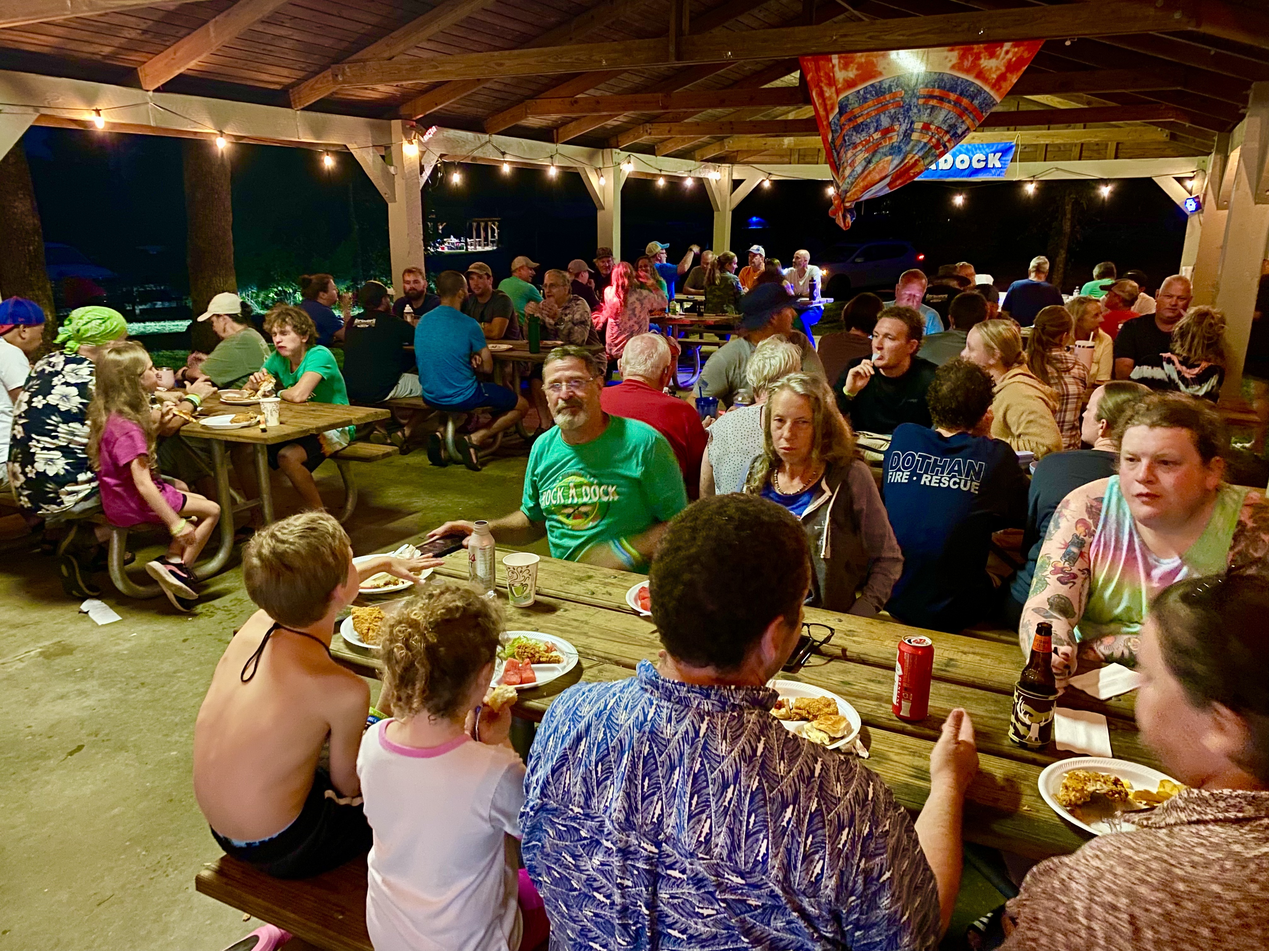 A large RockADock group sharing an evening meal beneath a lighted outdoor pavilion