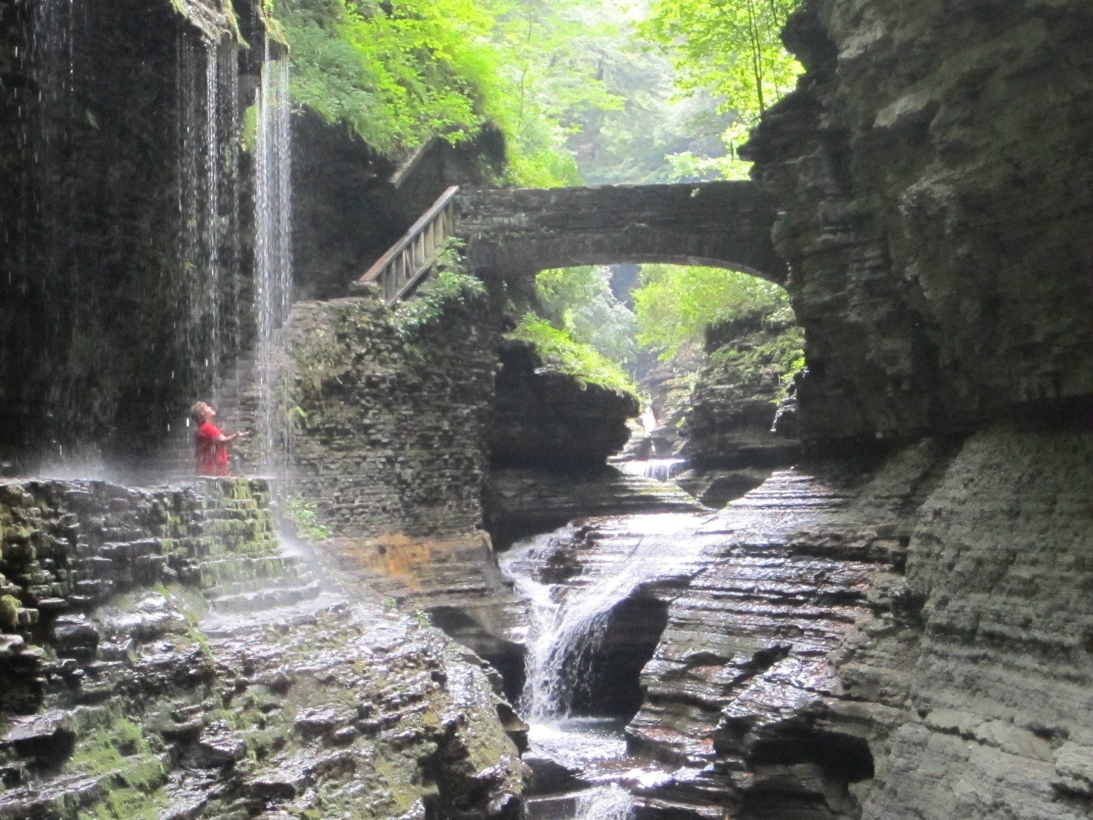 A stone bridge and waterfall framed by the narrow gorge walls.