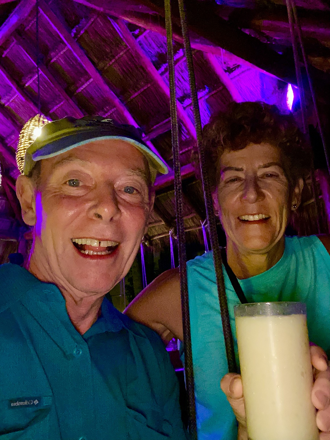 A cheerful nighttime drink beneath purple lights at a tropical open-air bar.