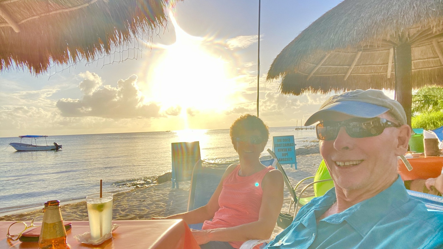 Drinks at a beachside table as the sun sets over calm tropical water.