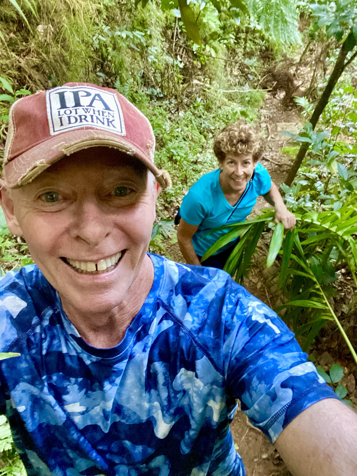 Tim and Kym climb a narrow jungle trail surrounded by lush tropical vegetation.
