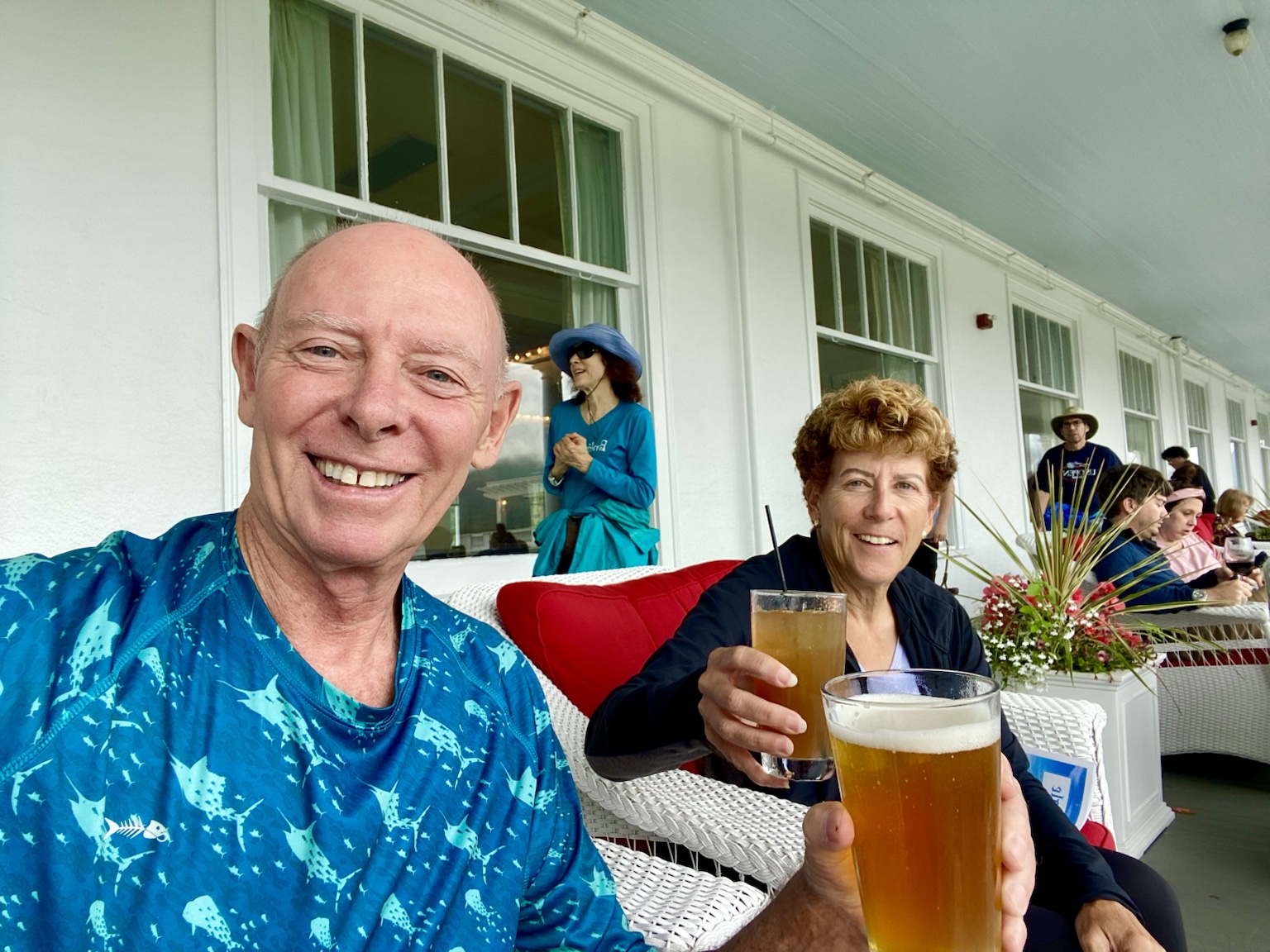 Tim and Kym raise their drinks on the veranda of a grand waterfront hotel.