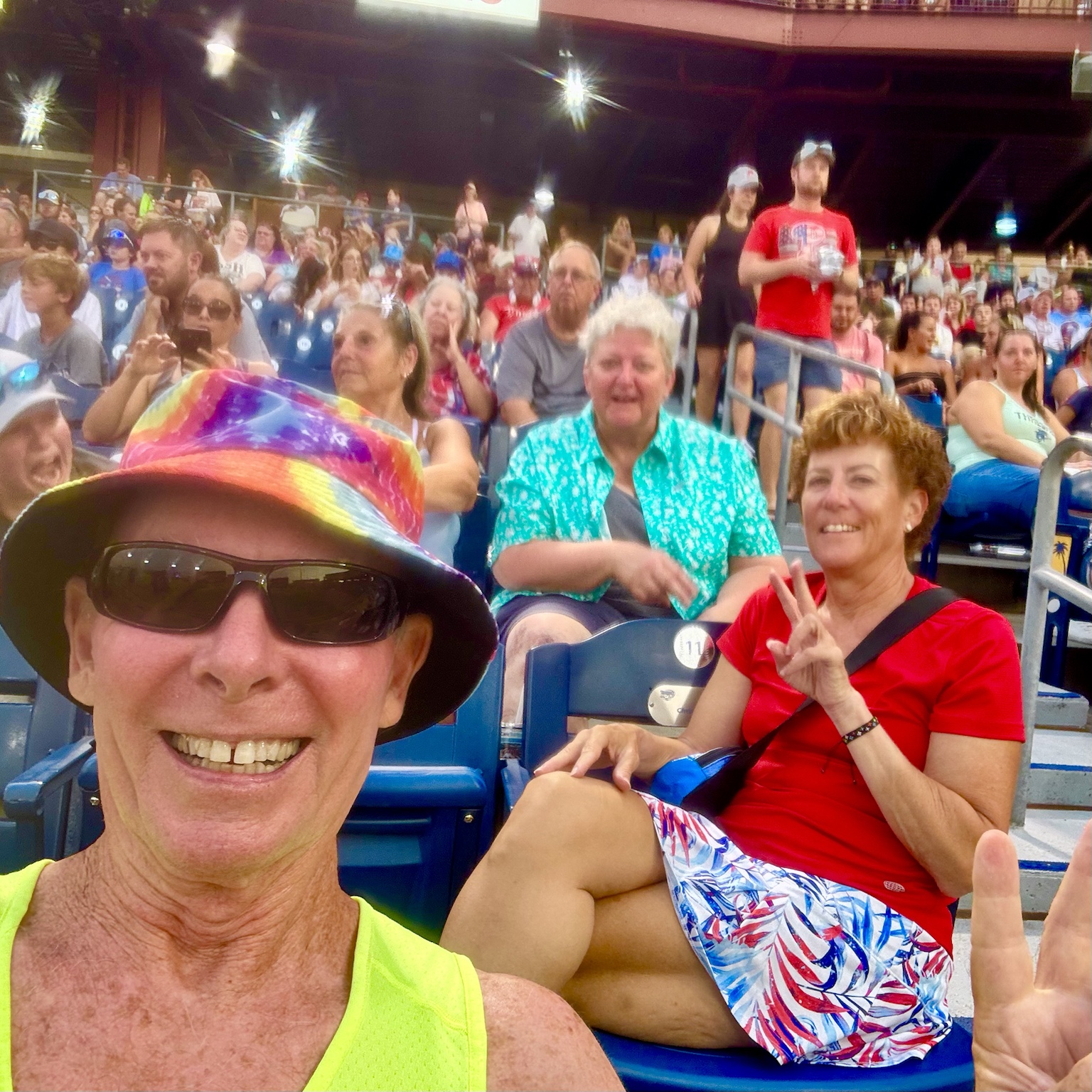 At a crowded sporting event with friends, dressed in bright colors and flashing peace signs.