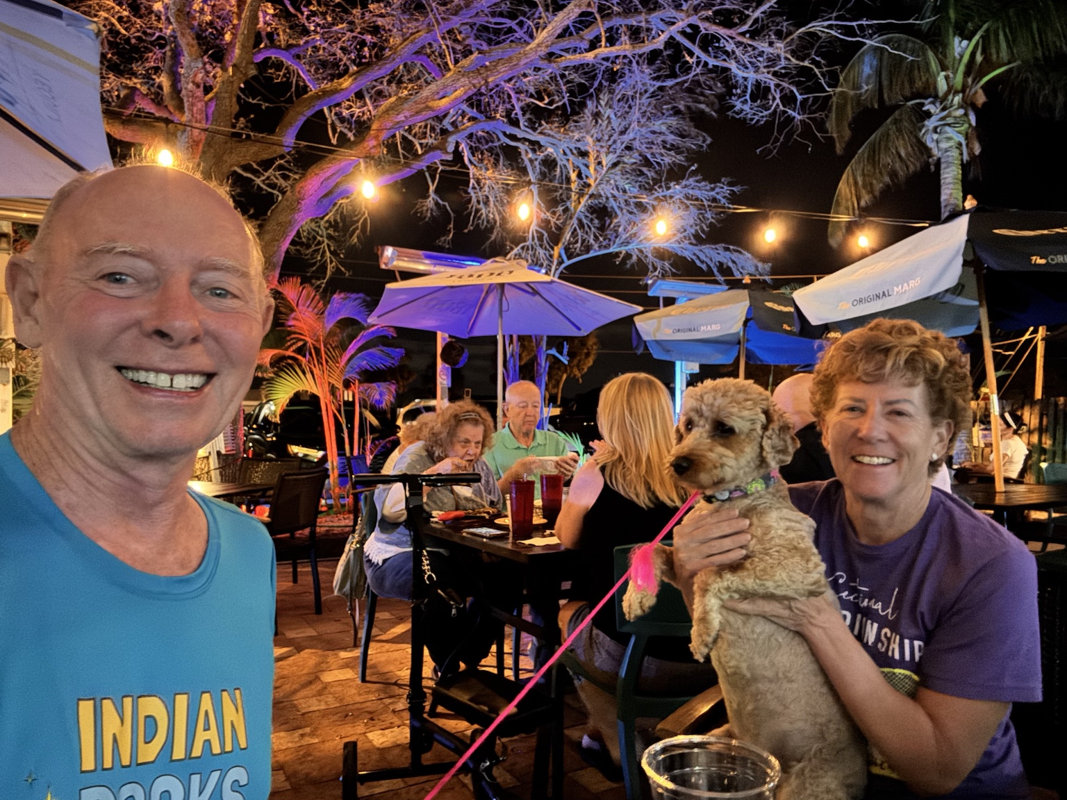 Tim, Kym, and Buddyboy enjoying a colorful evening at an outdoor restaurant.