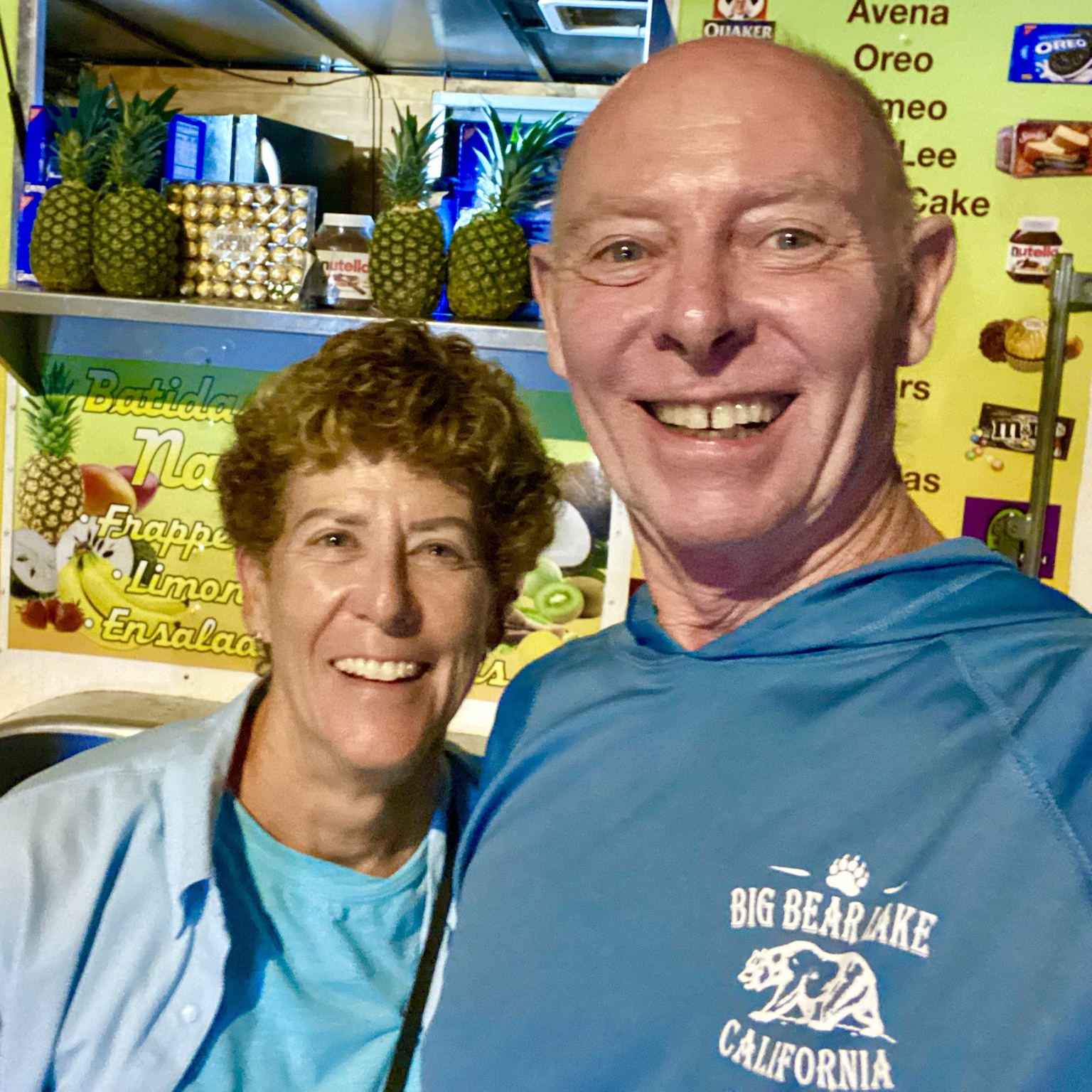 A cheerful selfie at a colorful fruit-drink stand decorated with pineapples.