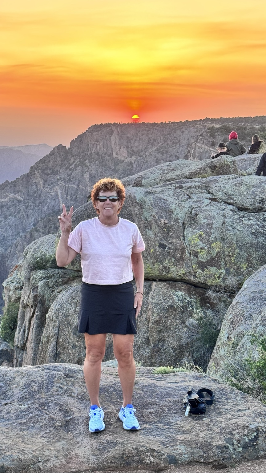 A second view of Kym at the rocky sunset overlook, with the mountains glowing behind her.