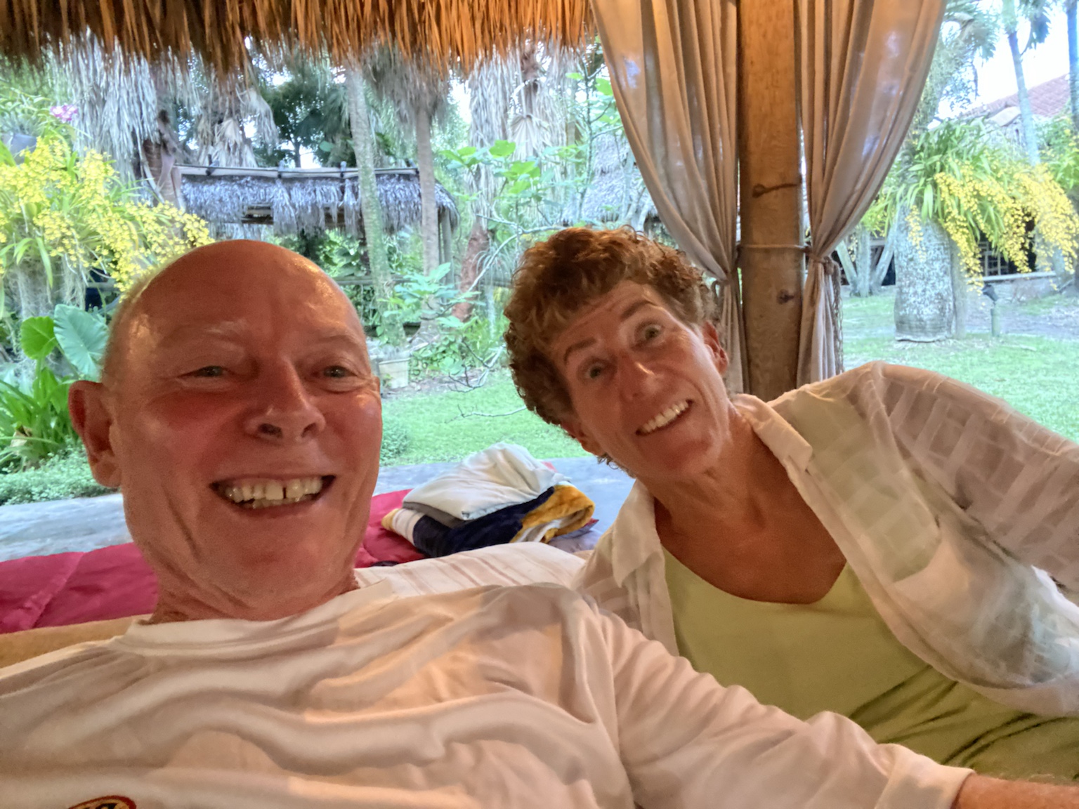 Relaxing together beneath a thatched roof in a tropical garden setting.