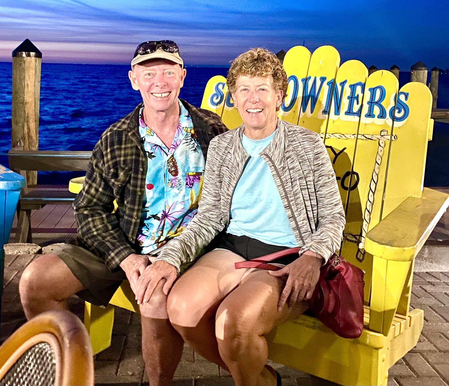 Tim and Kym seated on a giant yellow chair beside the water at sundown.