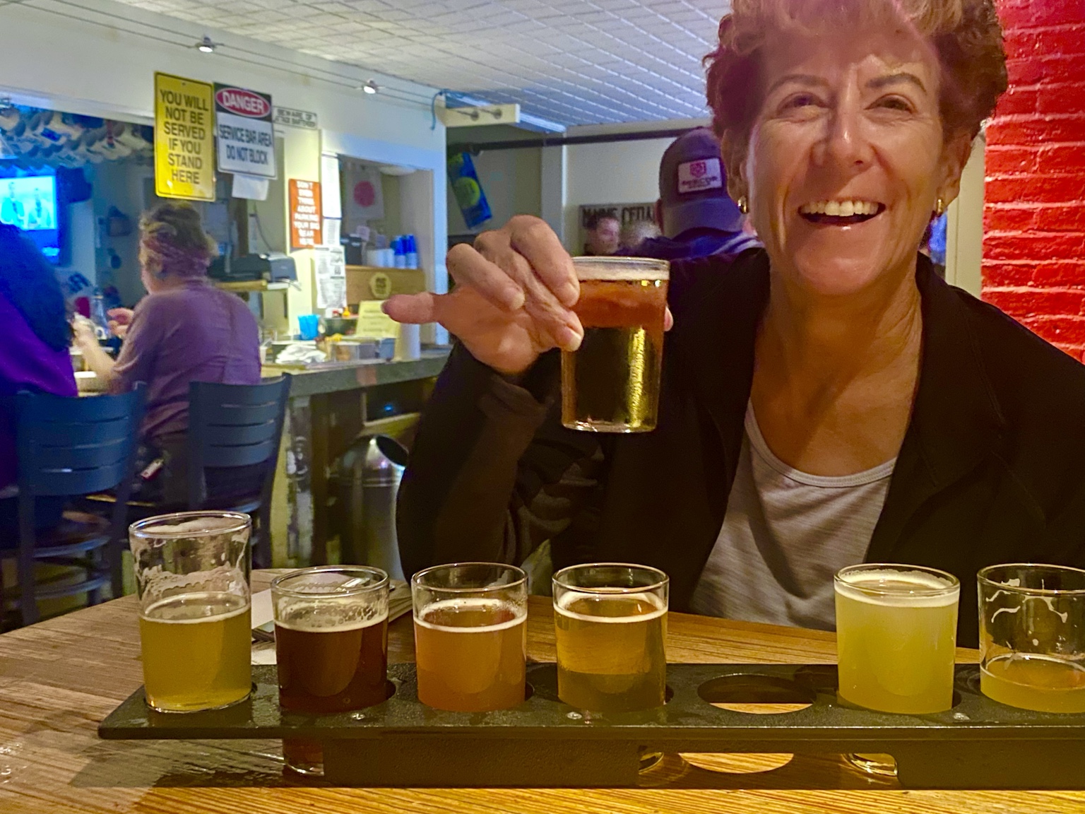 Kym samples a flight of craft beers, holding one glass up for the camera.