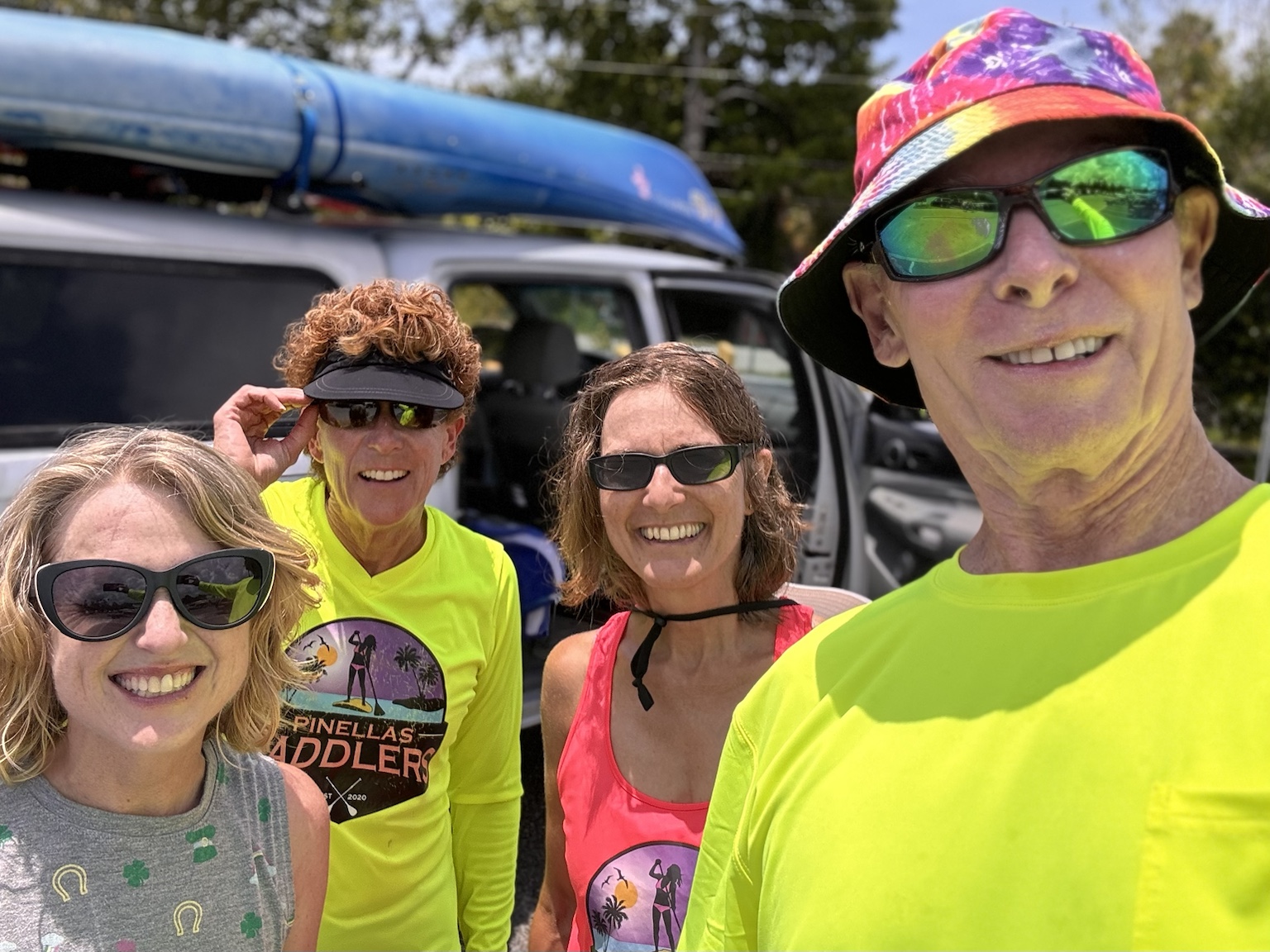A bright paddling-day group selfie beside kayaks loaded on the vehicle.
